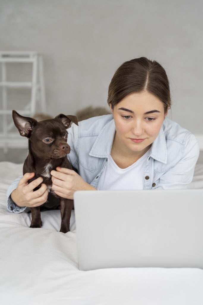 Pet owner conducting a telemedicine consultation with a veterinarian using a laptop, with a small dog sitting beside her.
